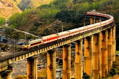 a red and white train traveling over a bridge next to a lush green mountain side