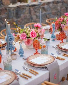 the table is set with pink and blue flowers, candles, and place settings for dinner