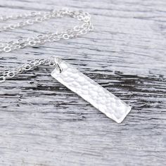 A modern take on a classic silver necklace. This necklace is specifically created to be just a whisper along your neck line, dainty, delicate, lightweight and beautiful. Perfect for layering with your favorite pieces. Elegant and dainty, this necklace consists of a vertical 1 inch Sterling Silver rectangle bar, hammered with my Classic texture and suspended from a dainty 1.9mm Sterling Silver cable chain. The pendant is suspended just over 1 inch in length from the chain. Bar Size: 1 Inch Neckla Elegant Silver Rectangular Bar Necklace, Minimalist Silver Chain Charm Necklace, Minimalist Charm Necklace With Silver Chain, Elegant Silver Hammered Charm Necklaces, Silver Minimalist Necklace With Rectangular Pendant, Minimalist Silver Hammered Charm Necklaces, Elegant Silver Hammered Charm Necklace, Simple Silver Necklace With Rectangular Pendant, Simple Silver Rectangular Pendant Jewelry