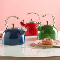 three tea kettles and a plate with a donut on it sitting on a table