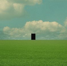 an open door in the middle of a green field with clouds above it and a blue sky filled with puffy white clouds