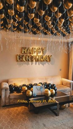 a living room filled with lots of balloons and black and gold balloons hanging from the ceiling