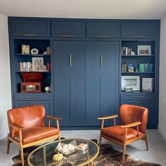 two chairs and a coffee table in a room with blue bookcases on the wall