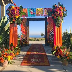 an archway decorated with flowers and orange drapes on the side of a road next to some plants