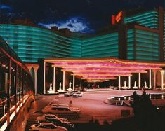 cars are parked in the parking lot near some tall buildings at night with colorful lights on them