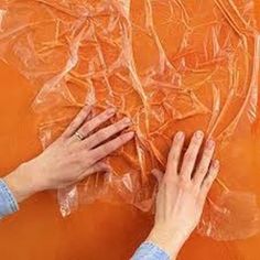 two hands are working on an orange piece of art with plastic wrap around the edges