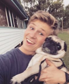 a young man holding a small dog in his arms and smiling at the camera while outside