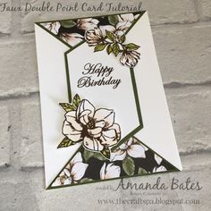 a birthday card with white flowers and green trimmings on a brick wall background