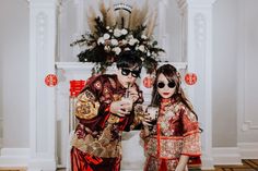 a man and woman dressed in traditional chinese garb standing next to each other holding drinks