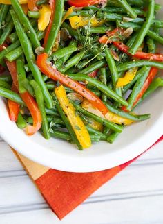 a white bowl filled with green beans and carrots on top of a red napkin