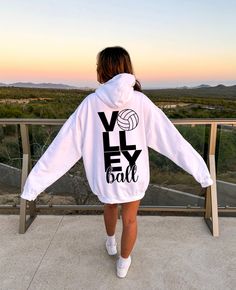 a woman wearing a white hoodie with the word volleyball printed on it, standing in front of a railing