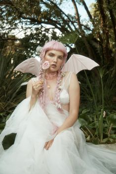 a woman with pink hair wearing a white dress and holding a flower in her hand