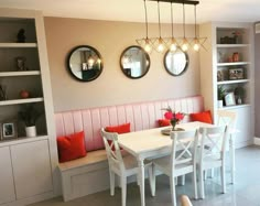 a dining room table with white chairs and red pillows on the bench next to it