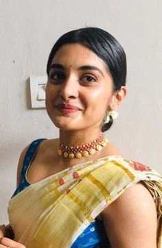 a woman wearing a yellow and blue sari with gold jewelry on her neck, smiling