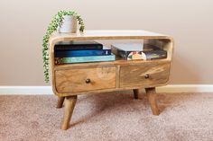 a small wooden table with two drawers and books on the bottom shelf next to a potted plant