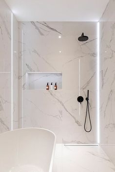 a bathroom with white marble walls and floor, along with a large bathtub in the corner