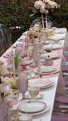 a long table is set with pink and white plates, cups, and saucers