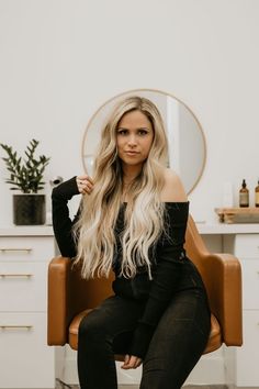 a woman sitting in a chair with long blonde hair and wearing black clothes, posing for the camera