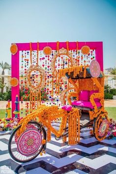 a bike decorated with orange and pink decorations in front of a large wall that has flowers on it