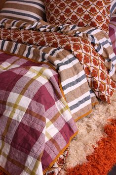 a bed covered in plaid and orange pillows on top of a white fluffy rug next to a wooden headboard