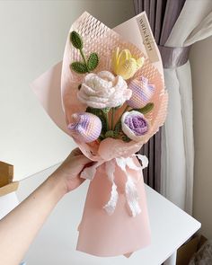 a person holding a bouquet of flowers on top of a white table next to a window