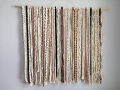 a wall hanging made out of different colored yarns on a white wall with a wooden hanger