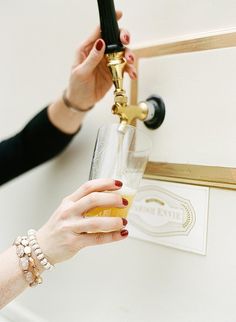 a woman is holding a beer glass in front of a wall mounted faucet