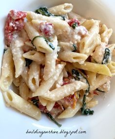 a white bowl filled with pasta covered in sauce and spinach leafy toppings