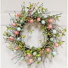 an easter wreath hanging on the front door with pink and blue eggs, green leaves and berries