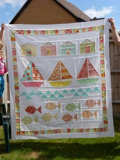 a person holding up a quilt in front of a house