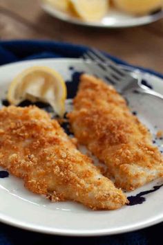 two pieces of fried fish on a plate with lemon wedges and a fork next to it