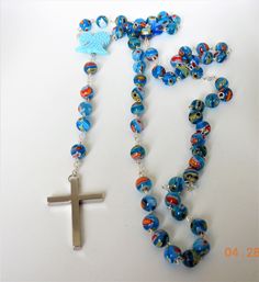 "This is a beautiful handmade traditional light blue bead Murano glass rosary/necklace with beautiful hand-carved \"real\" turquoise angel wings 20mm in size. This piece is a rosary necklace that is made out of stainless steel and authentic Murano glass beads. The glass beads are approximately 8 mm. The cross is stainless steel and all the connectors between each multi-stone bead are made out of stainless steel as well. The necklace measures 22 inches long with a 2\" cross. If you would like it Blue Crucifix Necklace For Spiritual Wear, Blue Crucifix Necklace For Spiritual Purposes, Turquoise Rosary With Round Beads As Gift, Handmade Blue Crucifix Jewelry, Handmade Blue Rosary For Jewelry Making, Blue Spiritual Rosary As A Gift, Twisted Ribbons, Traditional Light, Filigree Pattern