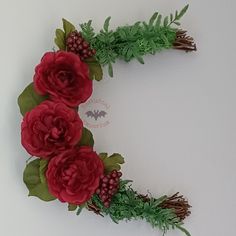 a wreath made out of red flowers and greenery on a white wall with bats in the background