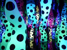 many different colored vases with black dots on them in a room filled with lights