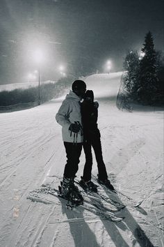 two people standing on skis in the snow at night with their arms around each other