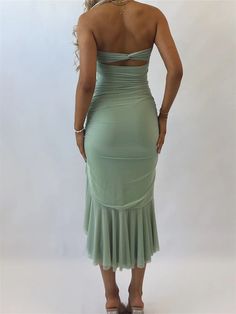 the back of a woman in a green dress with her hands on her hips, looking over her shoulder