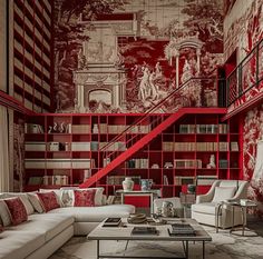 a living room filled with furniture and bookshelves next to a stair case covered in red wallpaper