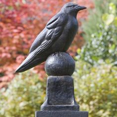 a statue of a bird sitting on top of a black post in front of some trees