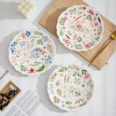 two plates with floral designs on them next to a recipe book