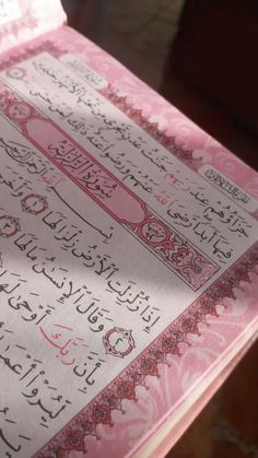 an open pink book with arabic writing on it's cover, sitting on a table