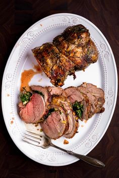 a white plate topped with meat and vegetables next to a fork on top of a wooden table