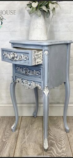 an antique blue painted table with drawers and flowers in a white vase on the top