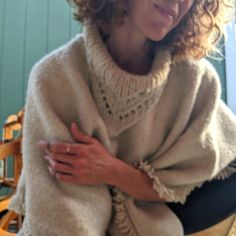 a woman with curly hair sitting on a chair wearing a ponchy shawl