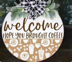 a welcome sign hanging from the side of a door with coffee cups and leaves on it