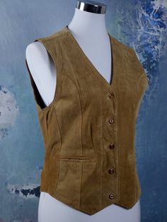 This vintage golden tan suede vest closes in the front with five buttons, and has two jetted pockets. The fully lined honey-colored pointed-front waistcoat features figure-enhancing contour lines on the front and a full leather back with a slip belt and a chevron slit on the center hemline. Brand label: Clic Point Size: Label: M, 6 US, 10 UK Material: Suede leather Condition: Excellent --- M E A S U R E M E N T S --- Bust = 34 inches (86.36cm) Vest Length Front = 23 inches (58.42cm) Vest Length Contour Lines, Leather Waistcoat, Label M, Suede Vest, Golden Tan, Brand Label, 1970s Fashion, 1960s Fashion, European Vintage