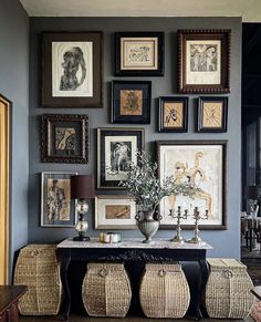 a wall with many pictures on it and two wicker stools next to the table