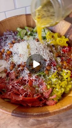 someone is pouring dressing into a salad in a wooden bowl on a counter top with other ingredients