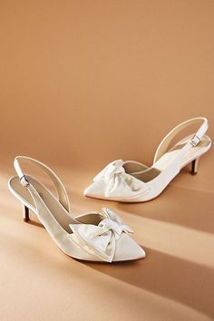 two pairs of white shoes with bows on the toes, one in satine and the other in leather