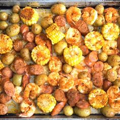 a tray filled with shrimp, potatoes and corn on the cob next to broccoli