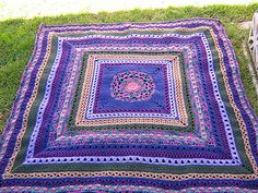 a crocheted blanket sitting on top of a green grass covered ground next to a bench